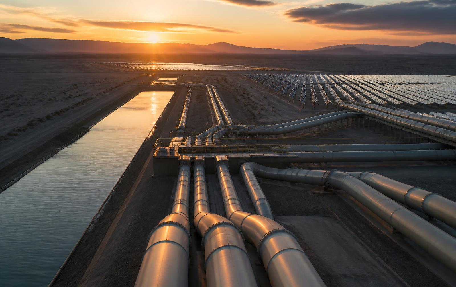 Desert water and energy facility with geometric pipelines and a solar field at dusk